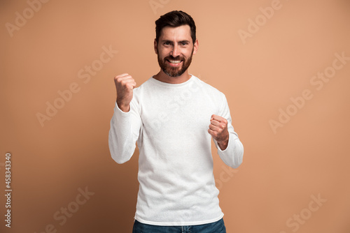 Portrait of ecstatic brunette man with beard showing yes i did it gesture and rejoicing copy space for ad. Indoor studio shot isolated on beige background