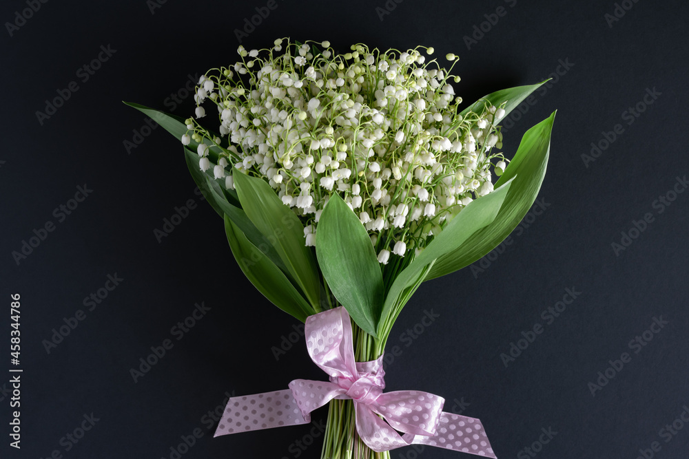 Happy holiday concept. A bouquet of beautiful fragrant white lilies of the valley on a dark background.