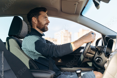 Low angle view of the serious confident man riding at the car and looking at the road during driving. Stock photo