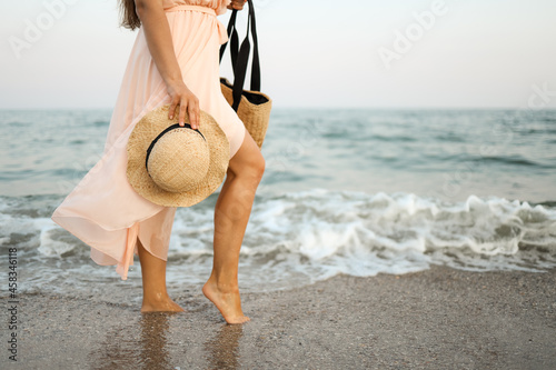 Woman in straw hat and pink dress on a tropical beach with brown bag.