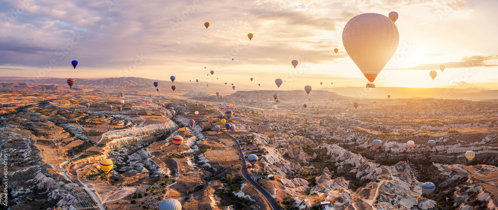 Hot air balloons flying above Göreme, Cappadocia (Kapadokya) Anatolia, Turkey at sunrise. Panoramic view of villages and fairy chimneys. Popular touristic destination for summer vacation holidays - obrazy, fototapety, plakaty 