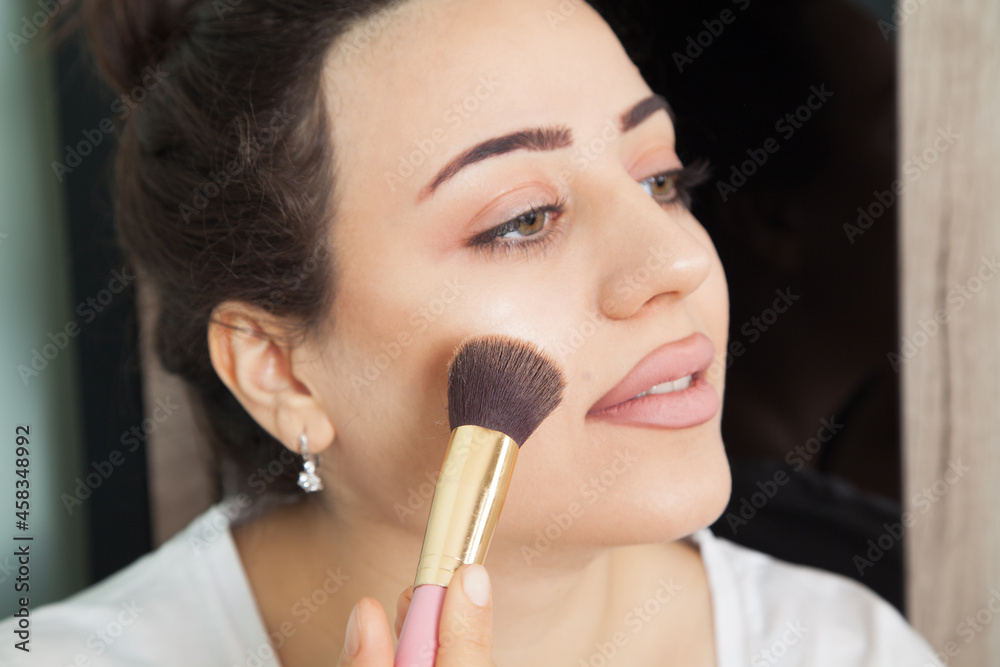 Young beautiful woman is wearing makeup. Fashion makeup and cosmetics. Makeup brush in a woman's hand. Young beautiful woman is wearing makeup. Fashion makeup and cosmetics. Makeup brush in a woman's hand.
