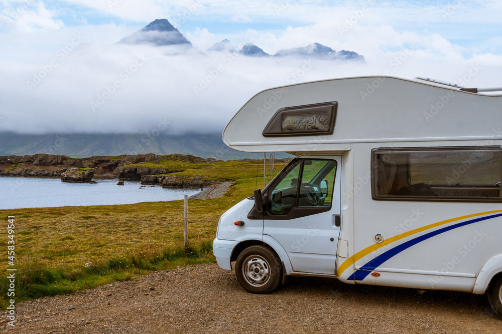 White RV in a viewpoint area in Berufjordur nearby Djupivogur. High cliffs of fjords are visible in the background, covered by low clouds in a typical summer day. East fjords, Iceland