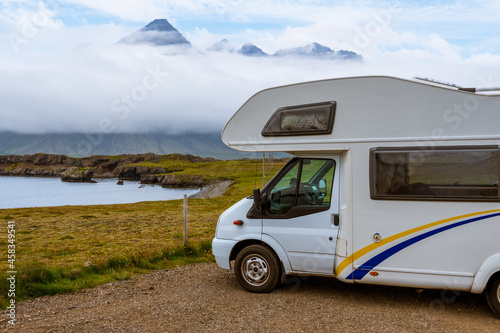 White RV in a viewpoint area in Berufjordur nearby Djupivogur. High cliffs of fjords are visible in the background, covered by low clouds in a typical summer day. East fjords, Iceland photo