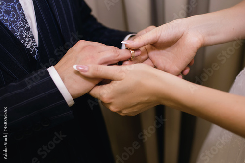 The bride puts a gold wedding ring on the groom's finger close-up. The bride gently holds the groom's hand and puts a ring on his finger at the wedding ceremony