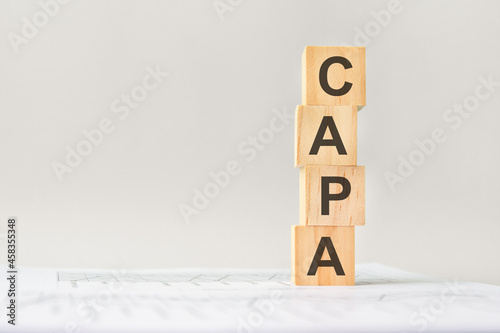 word CAPA with wood building blocks, light gray background. document with numbers on background, business concept. space for text in left. front view.