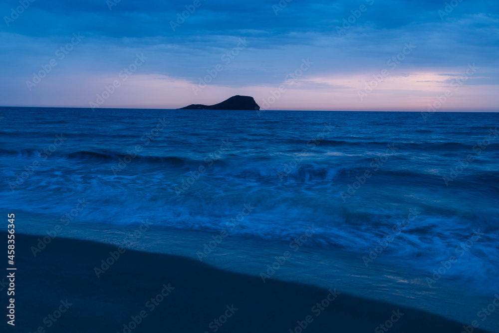 sunrise on a beach with an island at the bottom of the horizon with silky water