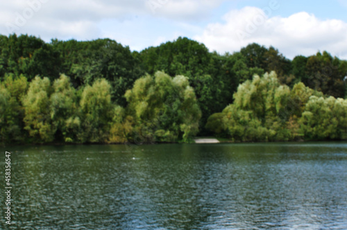 Blurred lake panorama background. Without focus, the water surface of the lake and the trees on the shore.