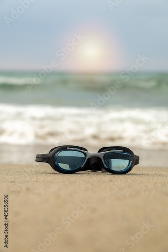 goggles for swimming in the water placed on the sand on the shore of the beach in a sunny sunrise