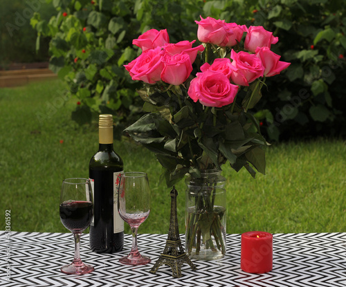 Bouquet of pink roses on an outdoor table with wine and candle - romantic setup photo