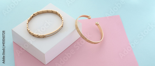 Slika na platnu Panorama of Two modern golden bracelets on pastel colors paper background with c