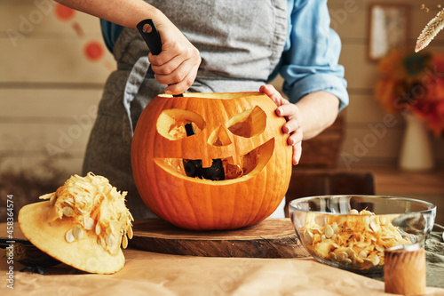 Fotografi Woman in apron standing in kitchen and removing all the pulp from Halloween pump