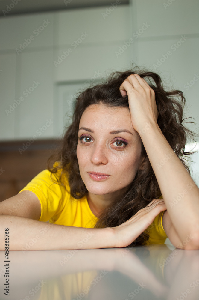 Beautiful curly girl in yellow t-shirt is looking at the camera at home in her apartment, posing with smile, happy people concept Beautiful curly girl in yellow t-shirt is looking at the camera at home in her apartment, posing with smile, happy people concept