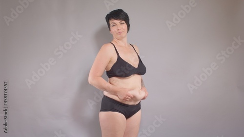 A woman bangs herself on the body with her hands, demonstrating excess weight on her stomach. Seeing yourself from the outside, motivation to diet and lose weight. Black underwear. photo