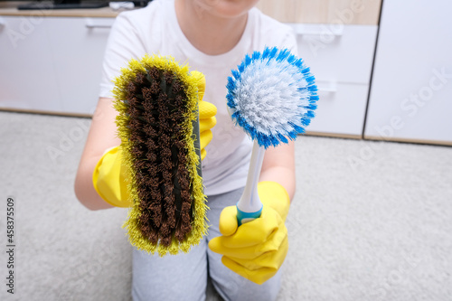 A child in yellow rubber gloves showing bruses for cleaning house, carpet from dust and stains photo