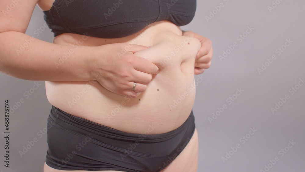 A woman touches her stomach with her hands, stretching the skin from adipose tissue. Body positivity, self-esteem enhancement. Weight loss motivation. A woman touches her stomach with her hands, stretching the skin from adipose tissue. Body positivity, self-esteem enhancement. Weight loss motivation.