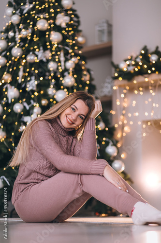 Happy woman sits by the fireplace near the Christmas tree decora