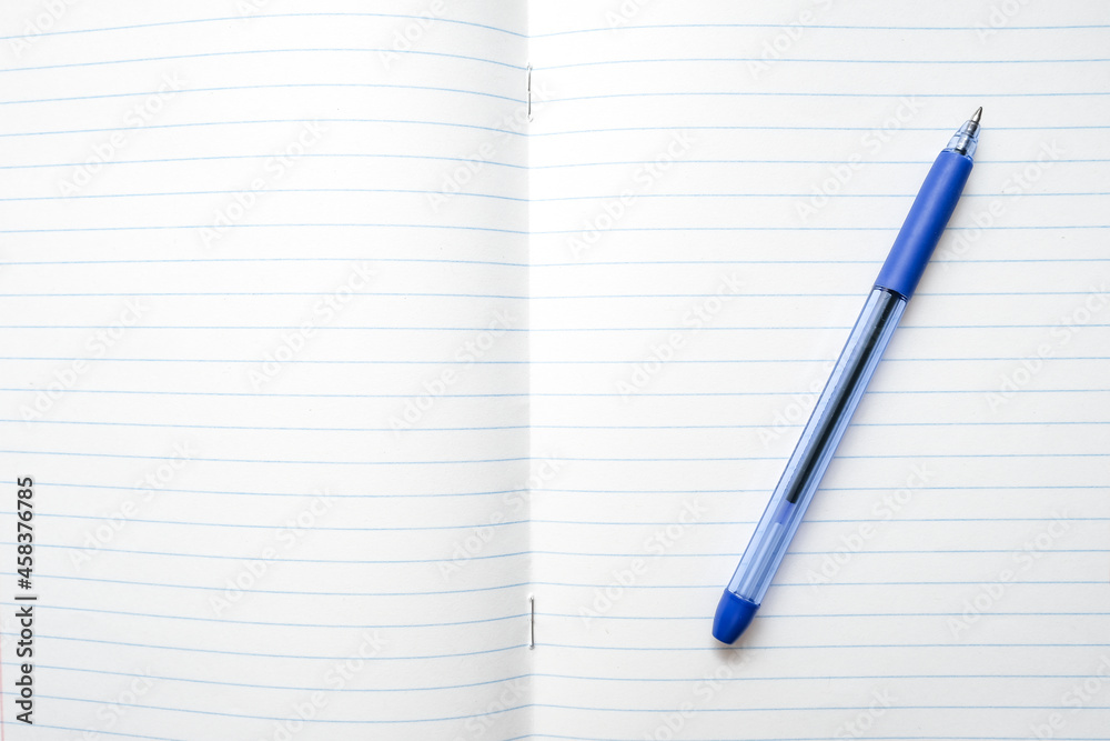 A blue ball pen lying on a blank lined school notebook sheet , paper with copy space A blue ball pen lying on a blank lined school notebook sheet , paper with copy space