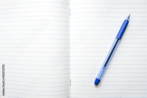 A blue ball pen lying on a blank lined school notebook sheet , paper with copy space