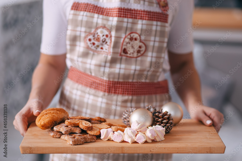 hands of a young girl - a cook in an apron holds a tray with bizet, cookies, toys, croissants. homemade baking