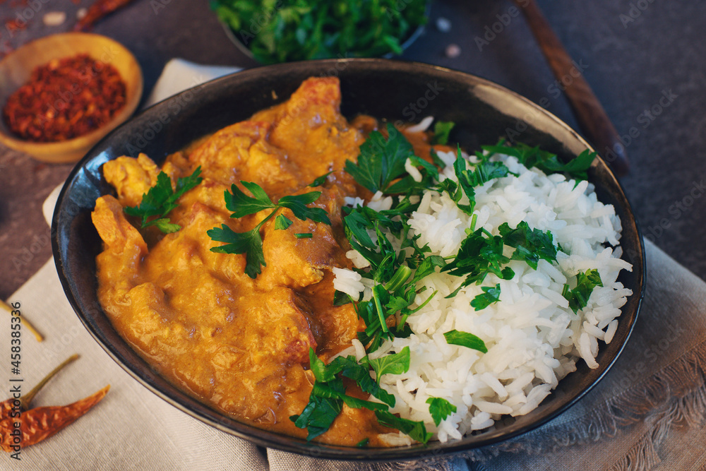 Traditional indian butter chicken in a bowl with basmati rice, spices and herbs