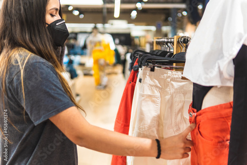 Young woman with face mask looking at clothes and doing shopping in a store
