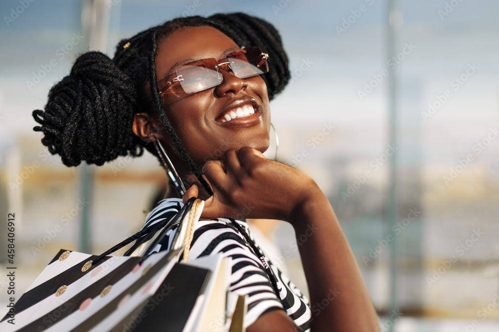 African American woman, wearing sunglasses, standing in a mall with shopping bags in her hands