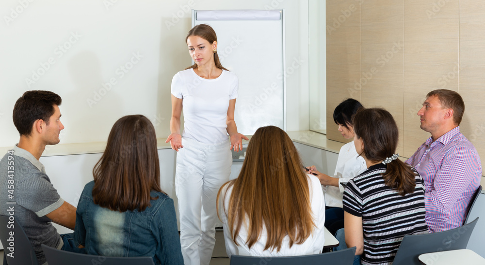 Positive young female business coach communicating with adult auditorium during training in office