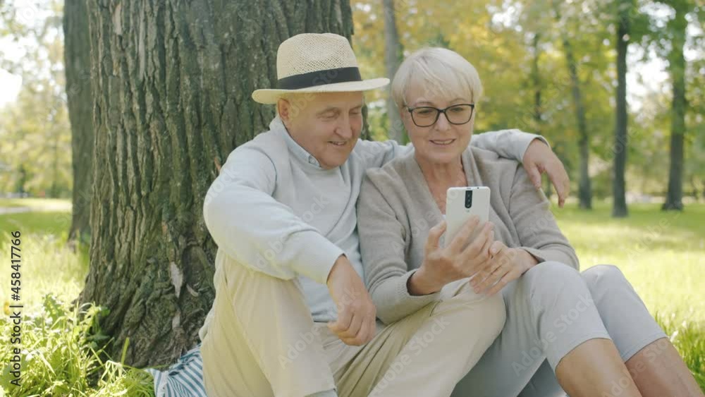 Smiling senior couple are making online video call talking and waving hand enjoying sunny day in green park. Smartphone and communication concept. Smiling senior couple are making online video call talking and waving hand enjoying sunny day in green park. Smartphone and communication concept.