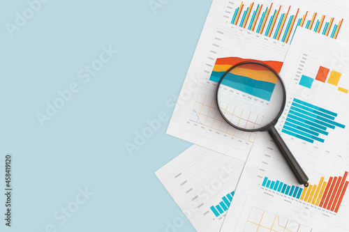Murais de parede Business graphs, charts and magnifying glass on table