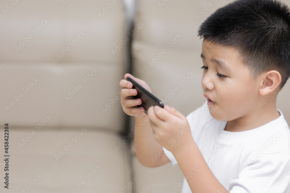 Happy little boy having fun playing game on mobile phone, Preschool kid sitting on sofa with smiling face watching cartoon on smartphone, Child using cell phone while relaxing at home Happy little boy having fun playing game on mobile phone, Preschool kid sitting on sofa with smiling face watching cartoon on smartphone, Child using cell phone while relaxing at home