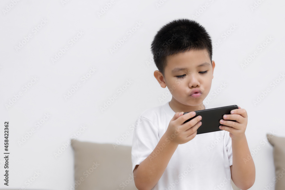 Happy little boy having fun playing game on mobile phone, Preschool kid sitting on sofa with smiling face watching cartoon on smartphone, Child using cell phone while relaxing at home Happy little boy having fun playing game on mobile phone, Preschool kid sitting on sofa with smiling face watching cartoon on smartphone, Child using cell phone while relaxing at home