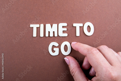 Time To Go. White letters of the alphabet and a woman's hand on a brown background