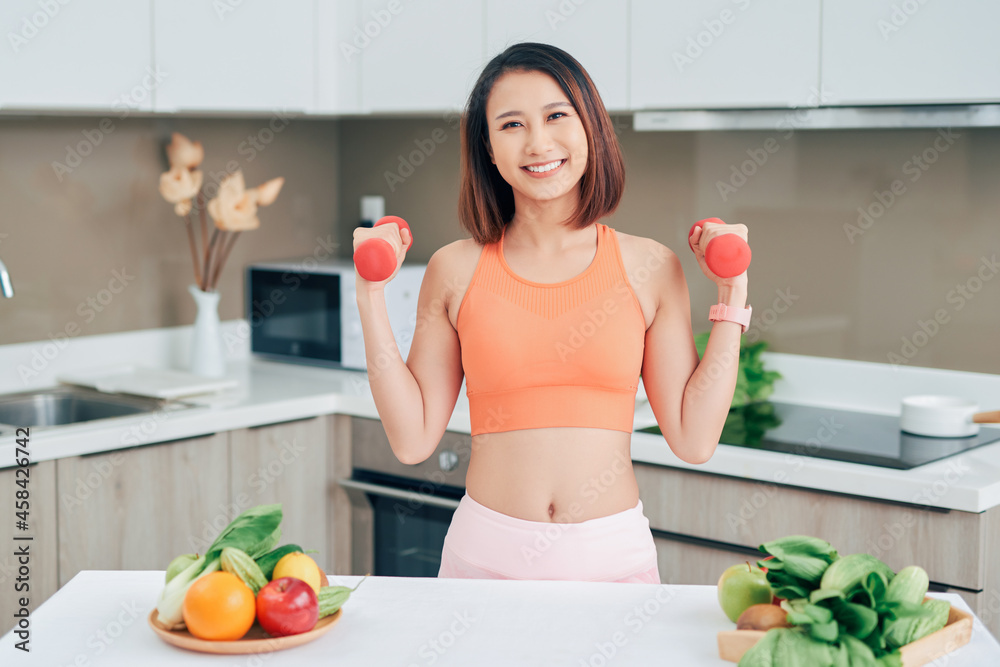 Young Asian woman holding dumbell and wearing sportive clother in kitchen Young Asian woman holding dumbell and wearing sportive clother in kitchen