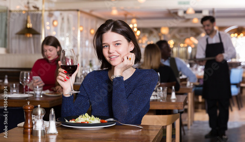 Happy girl enjoying delicious salad and red wine in stylish modern restaurant.