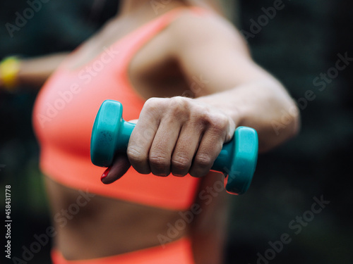 beautiful blond fitness model with long hair in neon orange activewear doing exercise with bar bells