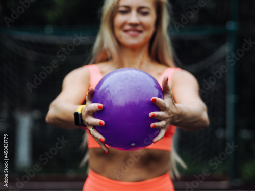 young beautiful blond fitness model with long hair in neon orange activewear doing exercise with ball