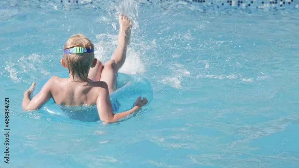 Little boy in swimming pool, child having fun, sitting on blue swimming ring, playing under water. Summer travel family hotel vacation tourists Little boy in swimming pool, child having fun, sitting on blue swimming ring, playing under water. Summer travel family hotel vacation tourists