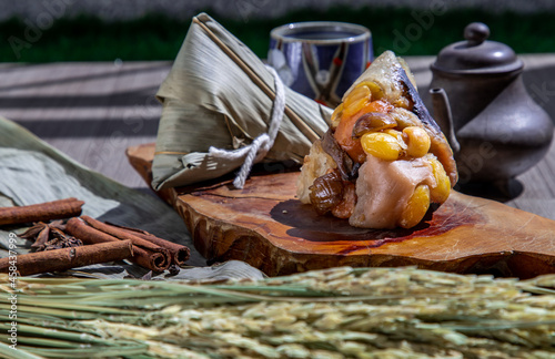 Chinese rice dumpling (Zongzi) shaped pyramidal wrapped by leaves ingredients on wooden plate Served with chinese tea and chopsticks. Famous asian tasty handmade food in dragon boat (duan wu) festival