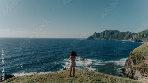 Back View Photo of Woman in Dress Standing on Cliff Near Body of Water