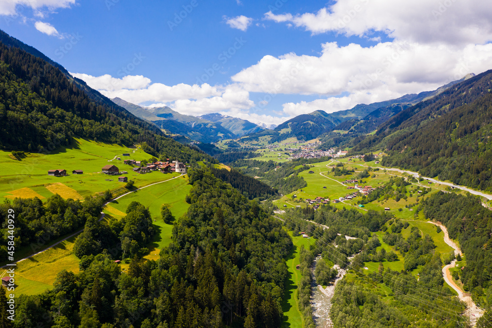 Picturesque aerial view of houses of small Swiss village Cavardiras in mountain valley in sunny summer day