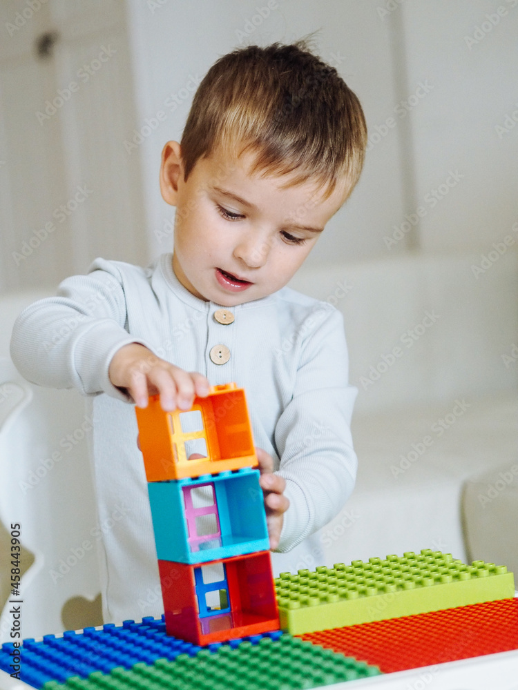 Cute toddler boy in beige clothes playing blocks in bright interioir Cute toddler boy in beige clothes playing blocks in bright interioir