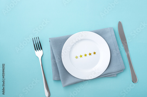 Five stars on white plate with fork and knife on blue background, food and service rating concept