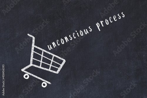 Chalk drawing of shopping cart and word unconscious process on black chalboard. Concept of globalization and mass consuming photo