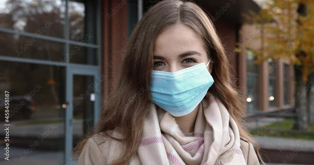 Waist up portrait view of the caucasian girl wearing protective mask looking at the camera while walking in the street during pandemic. Outdoor portrait of the happy female tourist Waist up portrait view of the caucasian girl wearing protective mask looking at the camera while walking in the street during pandemic. Outdoor portrait of the happy female tourist