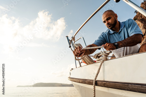 Print op canvas Young african american sailor tying ropes on sailboat in the sea on sunset