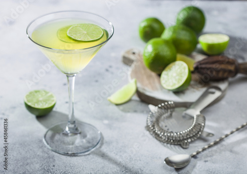 Bild auf Leinwand Gimlet Kamikaze cocktail in martini glass with lime slice and ice on light board with fresh limes and strainer with shaker