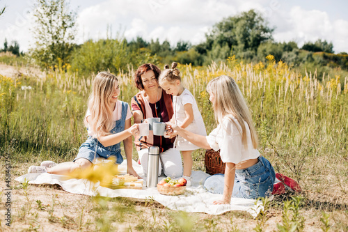 Three generations of women of the same family drink tea from mugs during a picnic in the park or on the lawn