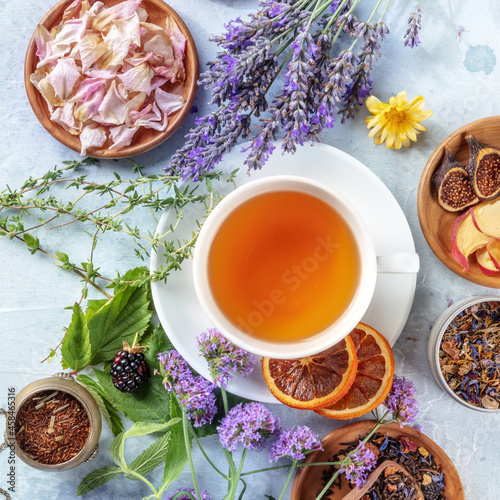 A cup of tea with dry fruit, flowers, and herbs, square overhead shot with lavender and oranges
