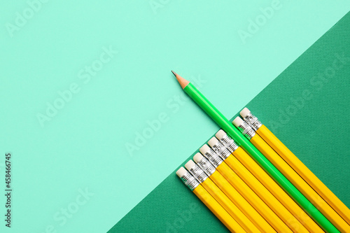 Green pencil among yellow ones on color background. Concept of uniqueness